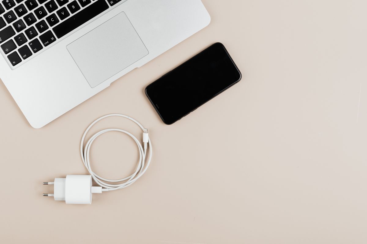 노트북 옆에 놓인 아이폰과 USB 케이블, 충전기
